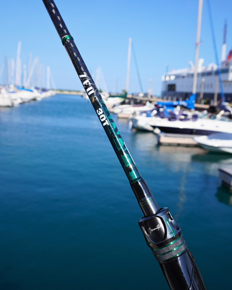 Carbon fiber fishing rod with dual tips shown in focus by a marina with boats in the background.