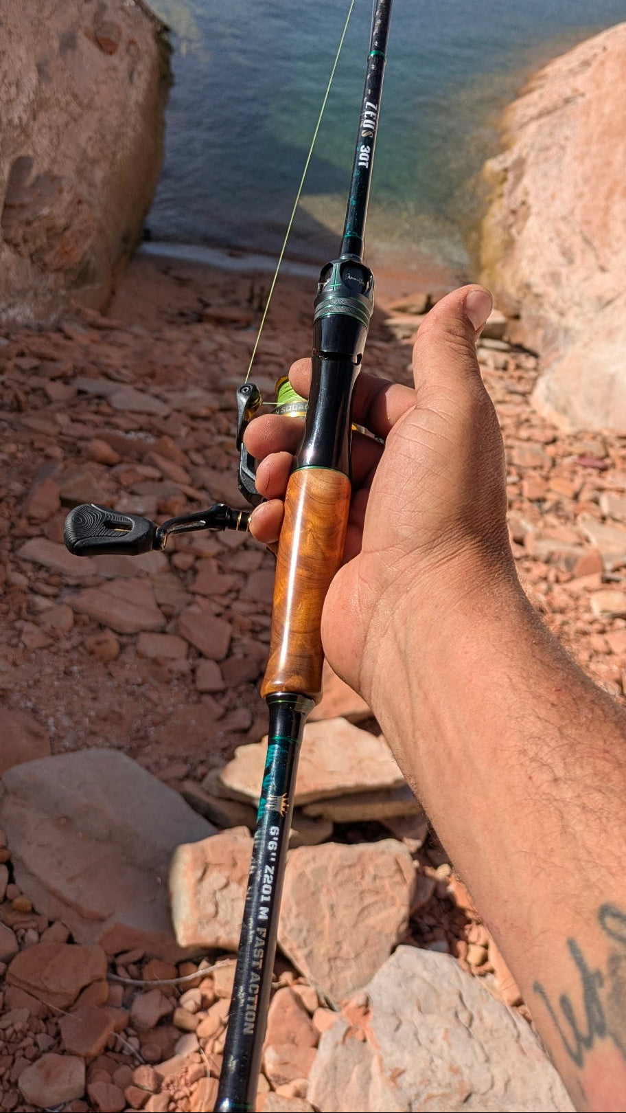 Hand holding a fishing rod by a rocky water body