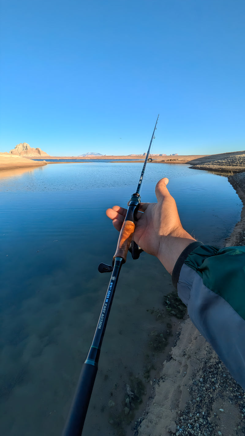 Angler holding carbon fiber fishing rod with wood handle beside clear blue lake