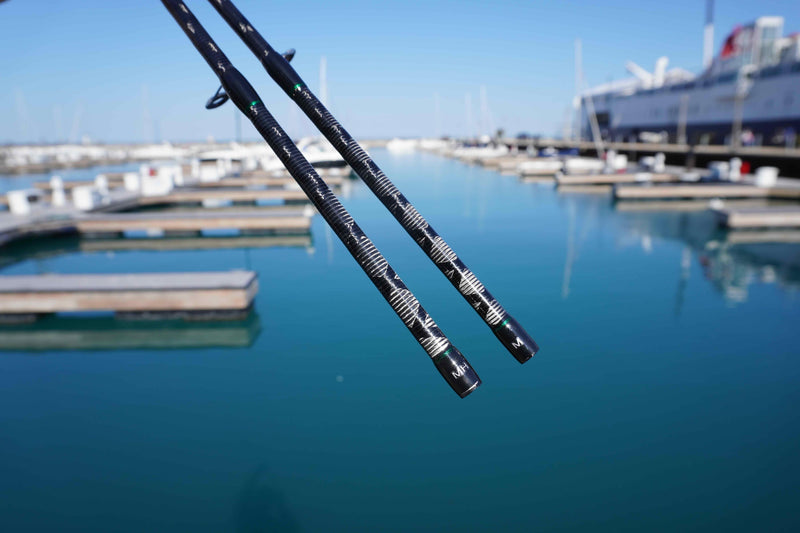 Close-up of dual-tip carbon fiber fishing rods at a marina with boats and docks in background